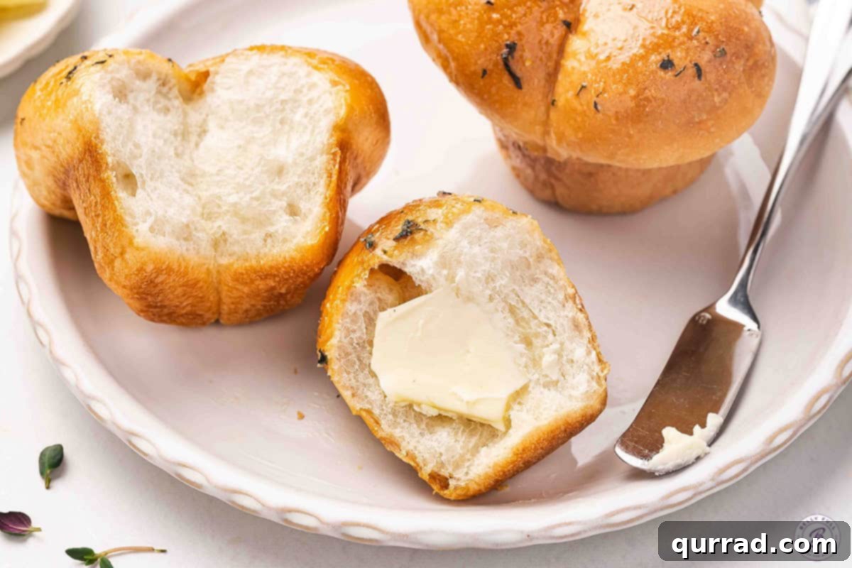Golden Pull-Apart Buns 11 A single cloverleaf roll on a plate, expertly sliced in half, revealing its fluffy interior, with a pat of butter melting perfectly inside, ready to be eaten.