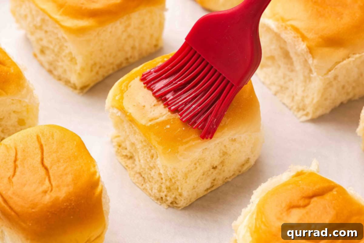 Boston Cream Pie Swirl Donuts 5 A hand brushing a Hawaiian roll with melted butter on a plate.