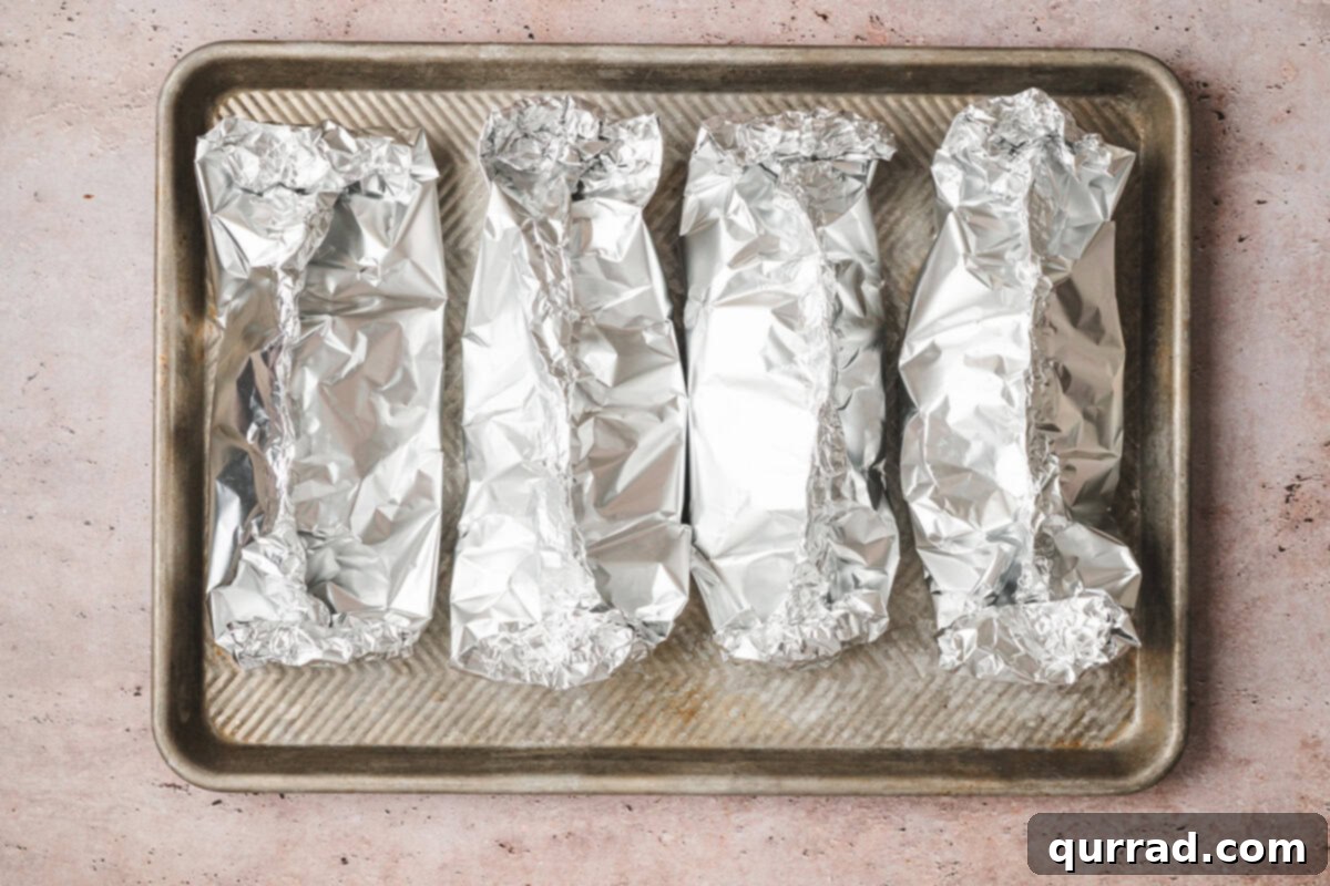 Four perfectly sealed Southwestern Chicken Foil Packets arranged on a baking sheet, ready for the oven.