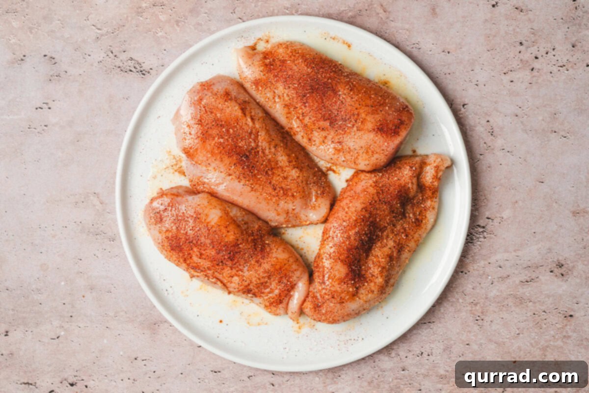 Four seasoned chicken breasts arranged on a plate, ready for the foil packets.
