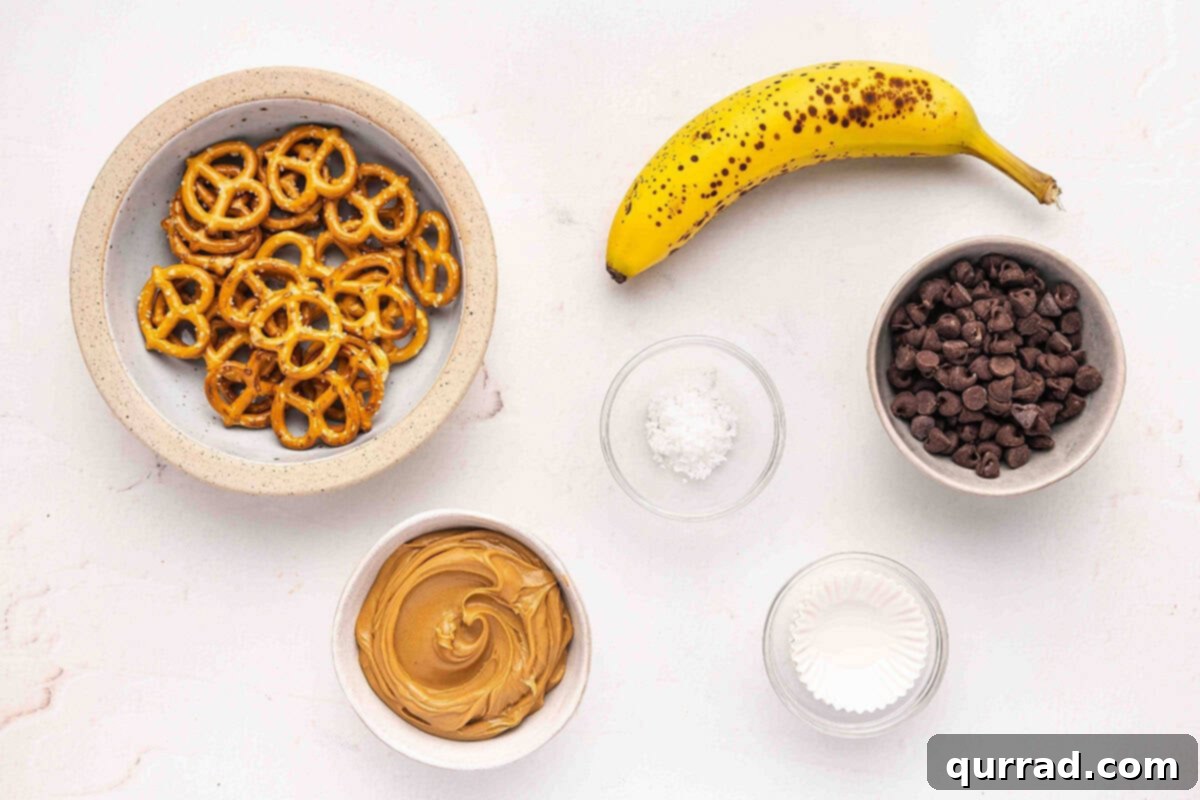 All ingredients laid out for making chocolate pretzel banana bites: pretzels, bananas, peanut butter, chocolate chips, and sea salt.