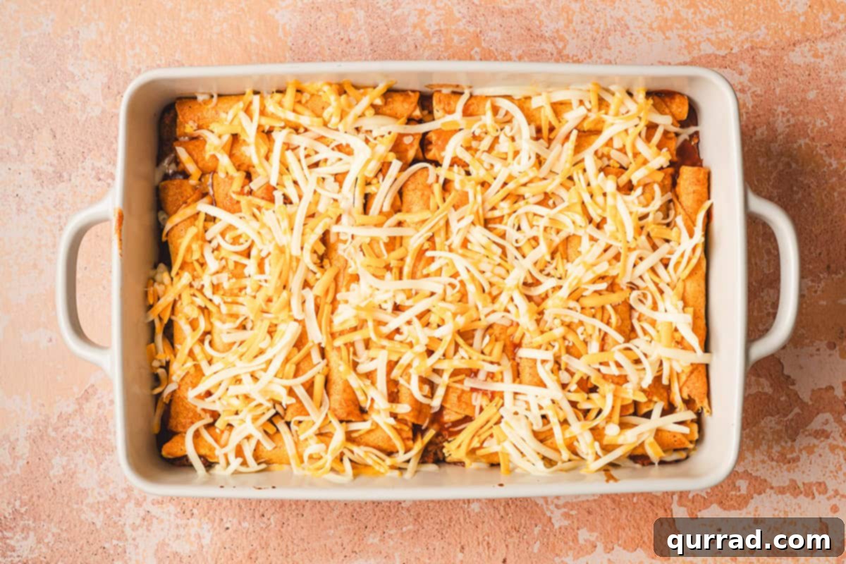 Effortless Enchilada Bake 9 A baking dish of partially baked lazy enchiladas with enchilada sauce, now topped with shredded Mexican blend cheese.