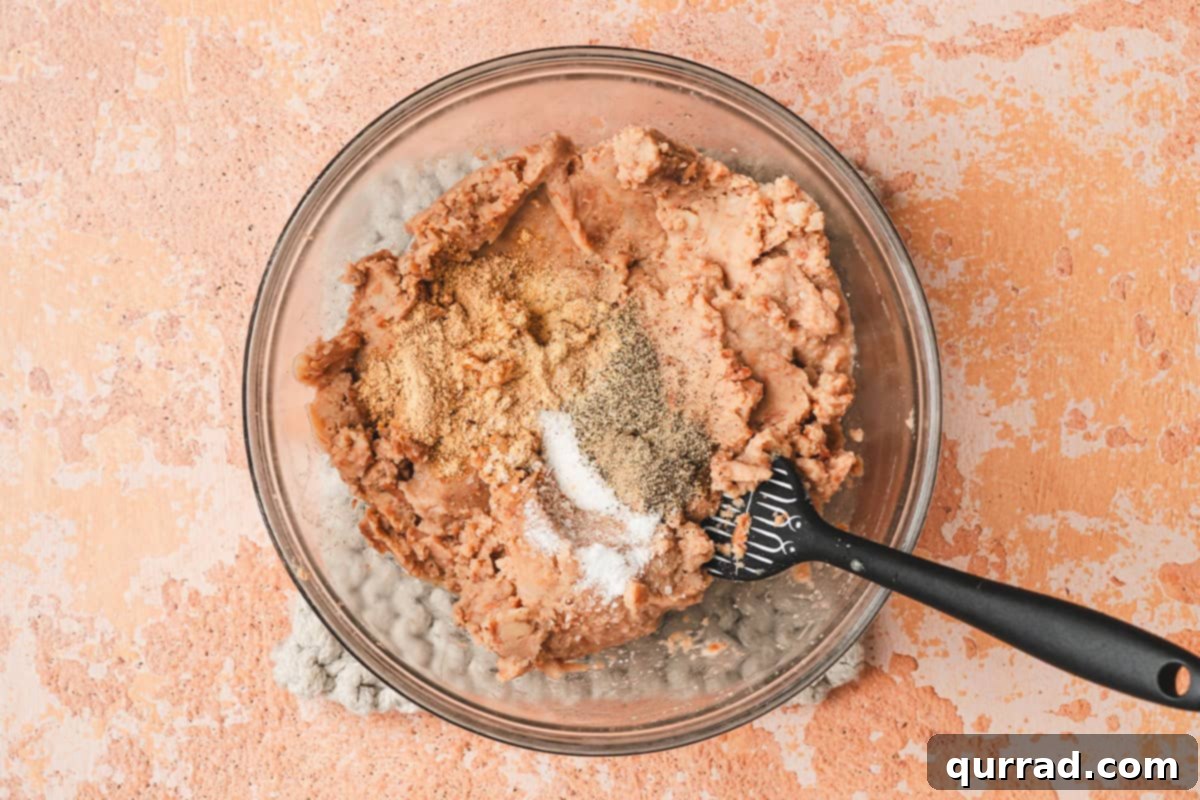 Effortless Enchilada Bake 5 Refried beans in a microwave-safe bowl seasoned with taco seasoning, garlic powder, salt, and pepper, ready to be mixed.
