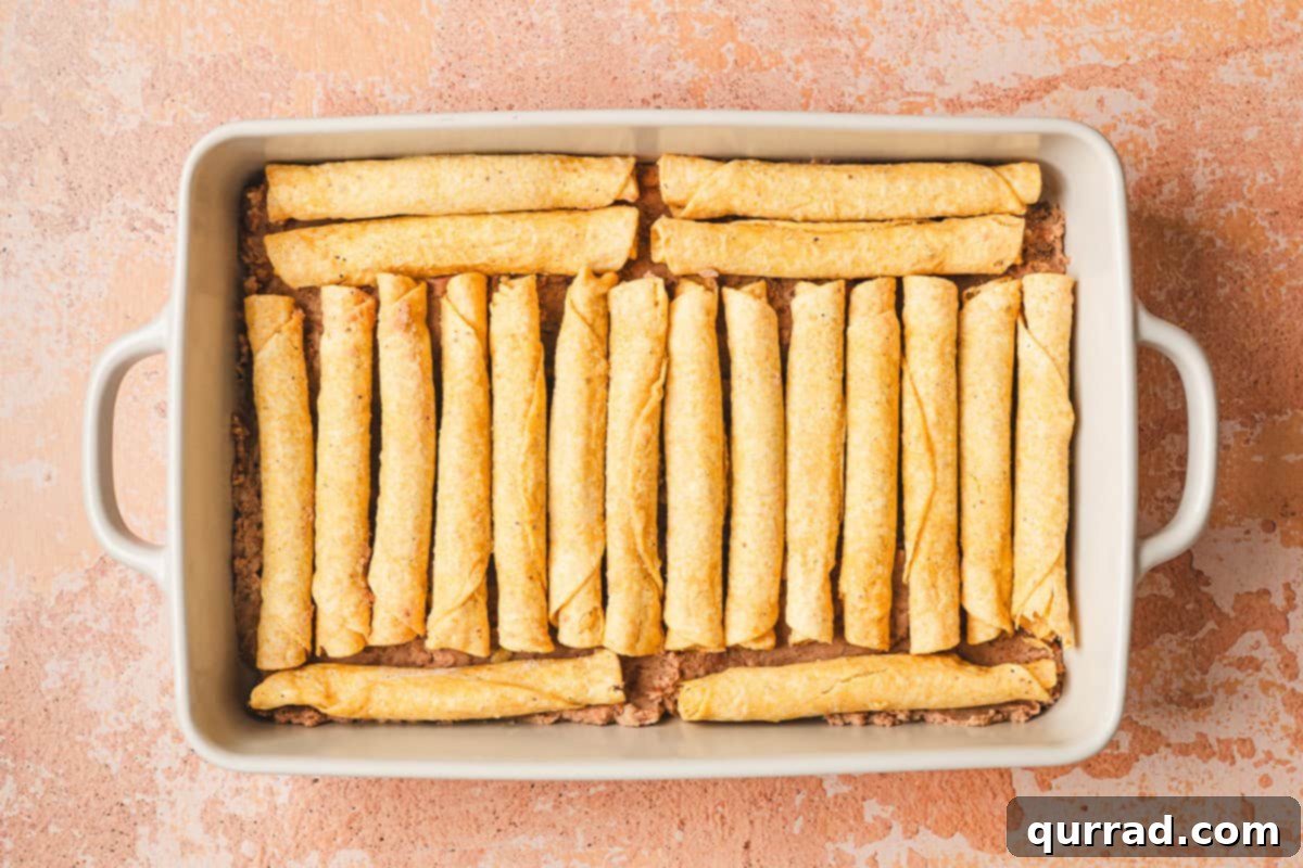 Effortless Enchilada Bake 7 Frozen taquitos neatly arranged in a single layer over the refried beans in the baking dish.
