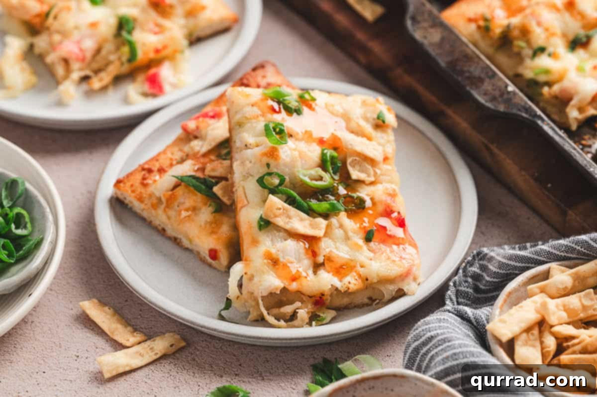 Crab Rangoon Pizza Delight 9 Two slices of crab rangoon pizza on a white plate, garnished with green onions and sweet chili sauce drizzle.