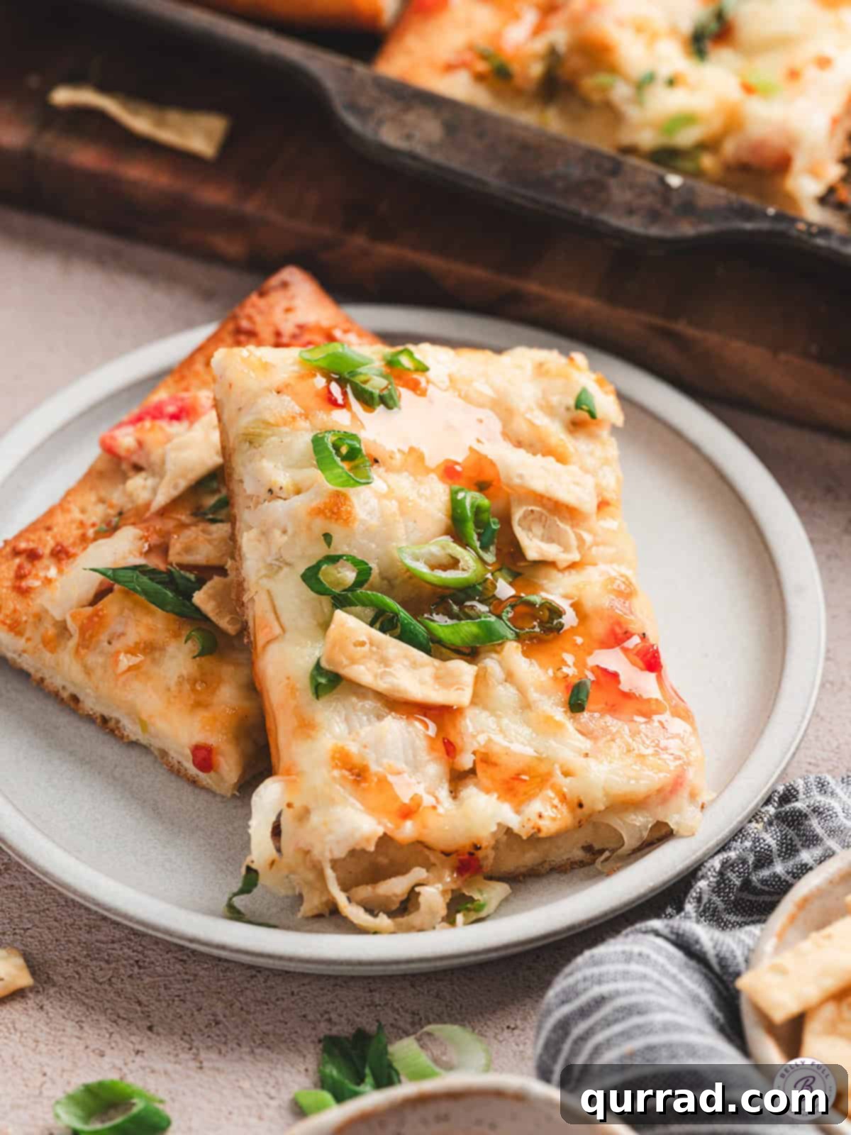 Crab Rangoon Pizza Delight 10 Two slices of crab rangoon pizza on a white plate, garnished with green onions and sweet chili sauce drizzle.