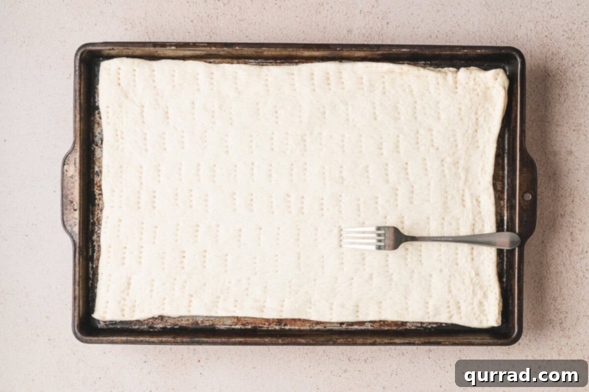 Crab Rangoon Pizza Delight 3 Rectangle of pizza dough pressed into a sheet pan and docked with a fork before baking.