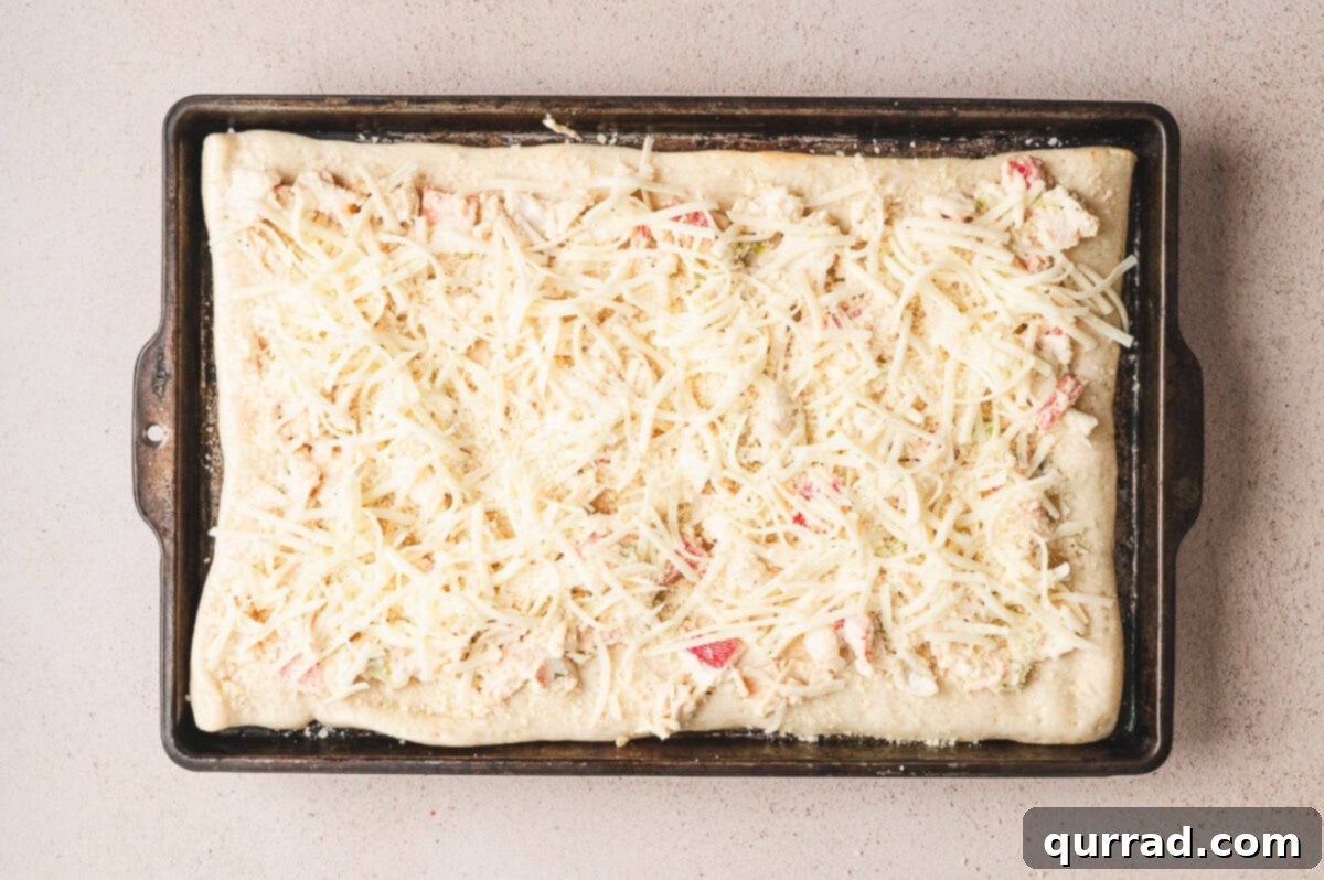 Crab Rangoon Pizza Delight 6 Unbaked crab rangoon pizza on a sheet pan topped with creamy crab mixture and shredded mozzarella.