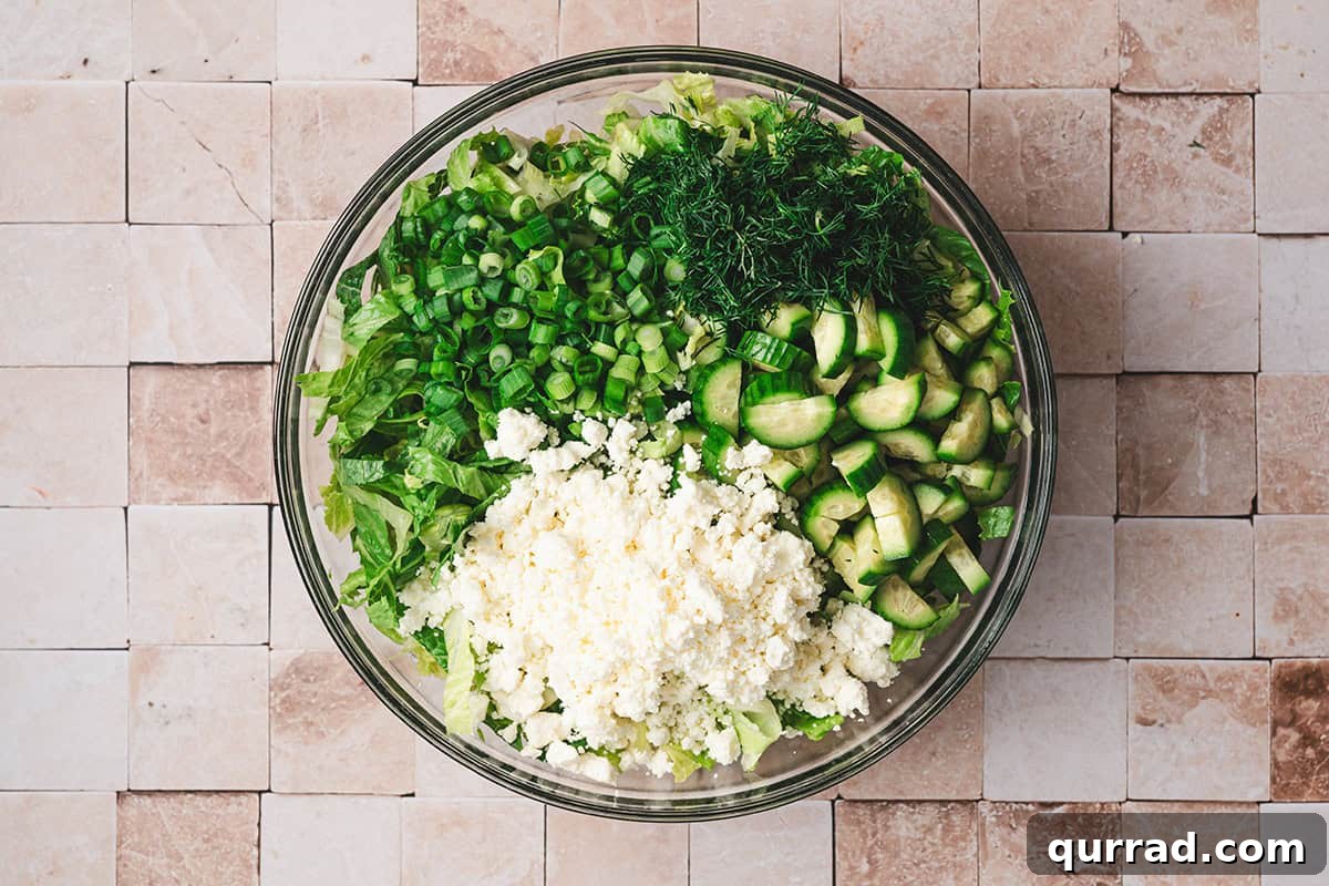 Crumbled feta, sliced cucumber, dill, green onions and lettuce in a bowl.