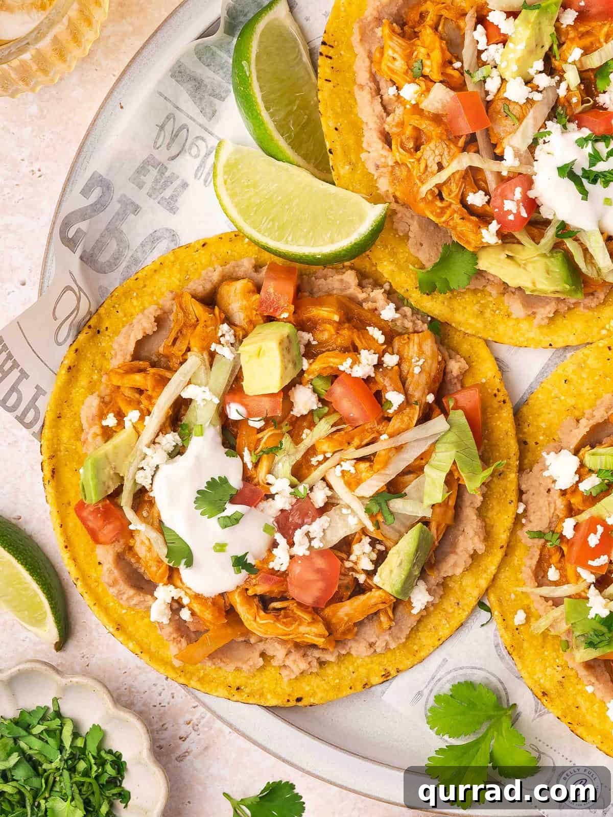 Overhead view of chicken tinga tostadas on a plate with cheese, sour cream and lime wedge toppings.
