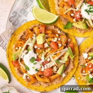 Overhead view of chicken tinga tostadas on a plate with cheese, sour cream and lime wedge toppings.
