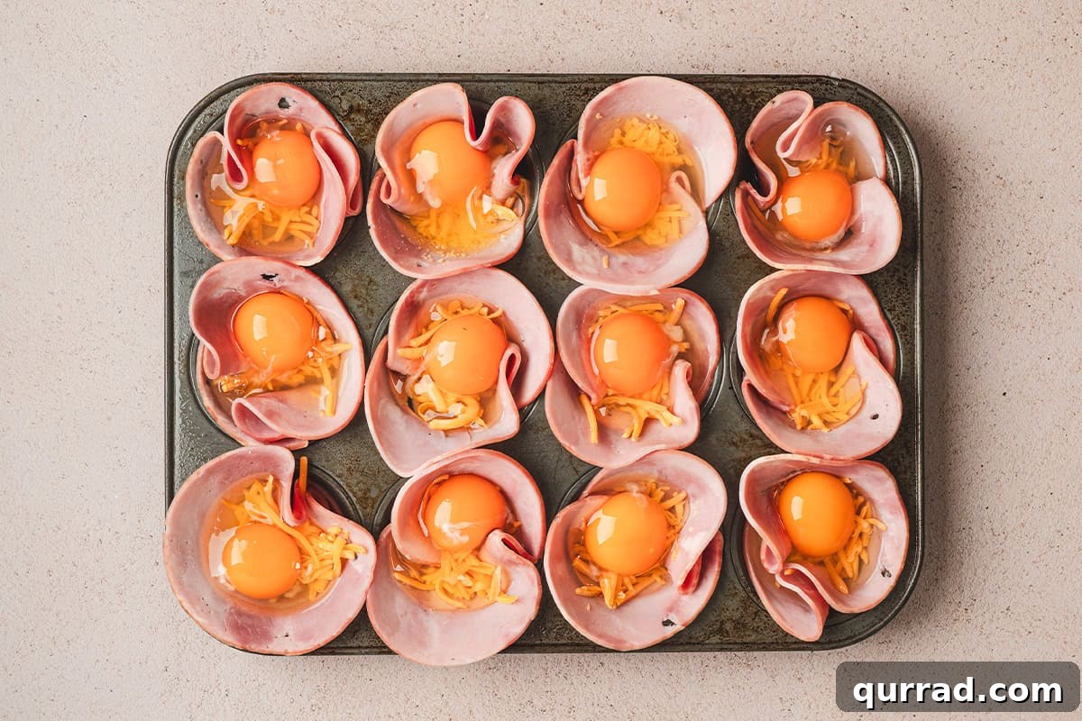 Savory Ham & Cheese Egg Cups for Quick Breakfast or Brunch 6 Ham placed in a muffin pan, with shredded cheese and eggs cracked on top.