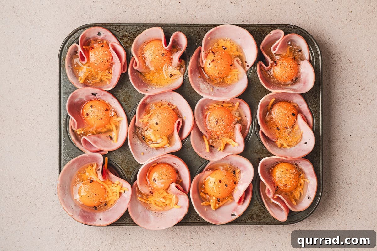 Savory Ham & Cheese Egg Cups for Quick Breakfast or Brunch 7 Ham placed in a muffin pan, with shredded cheese and eggs cracked on top with seasonings sprinkled over them.