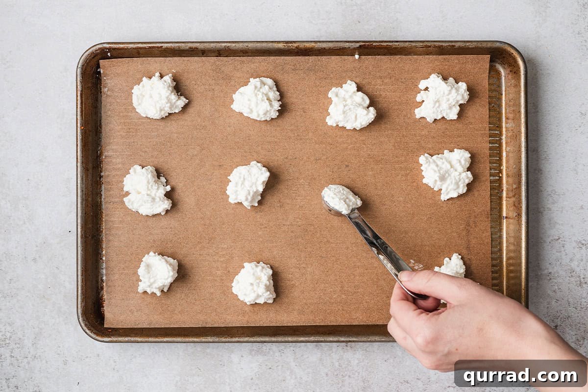 Cottage cheese being spooned onto a parchment lined baking sheet.