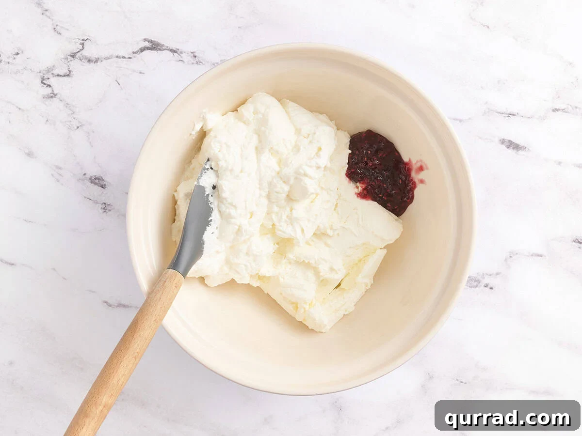 How to Make a Classic French Crepe Cake (Mille Crêpes) 8 A mixing bowl with softened cream cheese and a spoonful of raspberry jam before blending.