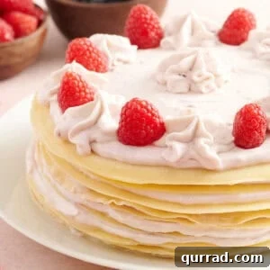 How to Make a Classic French Crepe Cake (Mille Crêpes) 3 A layered crepe cake filled with raspberry cream, topped with piped cream swirls and fresh raspberries, with bowls of blueberries and raspberries in the background.