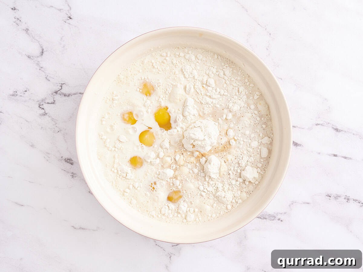 How to Make a Classic French Crepe Cake (Mille Crêpes) 5 A mixing bowl with eggs, milk, flour, sugar, and salt before mixing, sitting on a white marble surface.