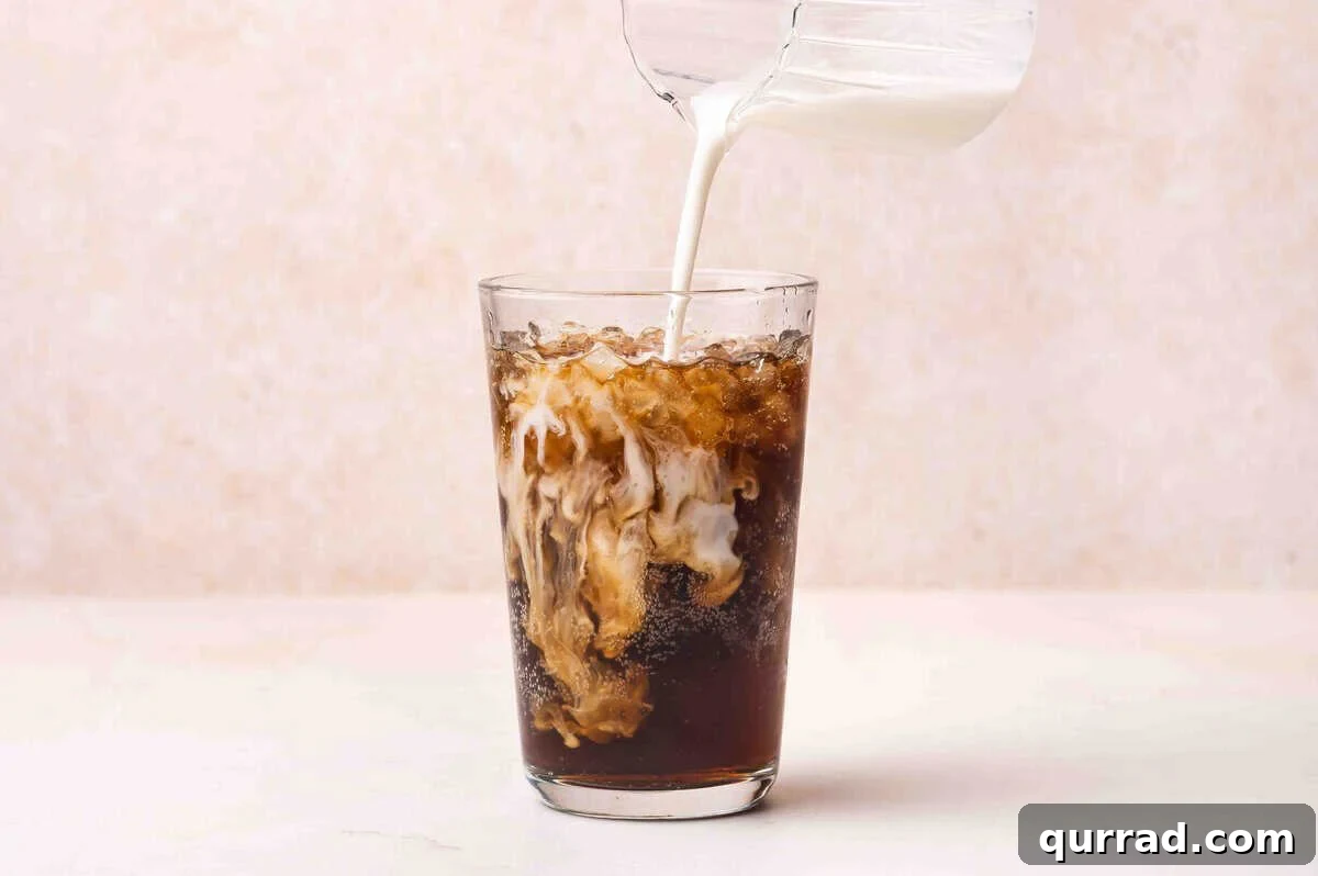 Coffee creamer being added to a glass of dr pepper.