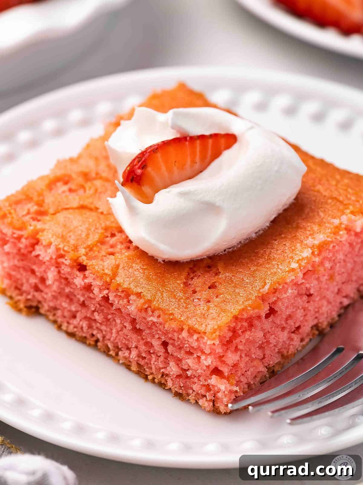 Moist Soda Cake Recipe with Creamy Vanilla Frosting 2 Side view of a slice of soda cake on a plate, topped with Cool whip and a strawberry.