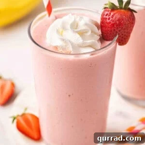 Creamy Strawberry Banana Orange Julius Smoothie 3 Side view of a glass of strawberry banana orange julius in a glass with whipped cream and a strawberry.
