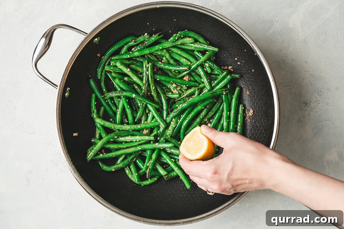 Garlic Green Beans Recipe: Sautéed with Lemon and Butter 8 A hand squeezing lemon over garlic green beans in a skillet.