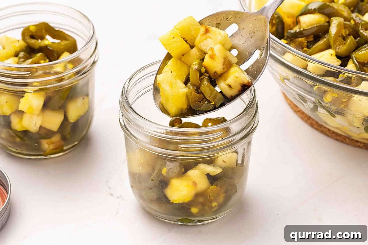 Cowgirl Candy Jalapeno Pepper Jelly Recipe 9 A slotted spoon adding jalapenos and pineapple to a glass mason jar.
