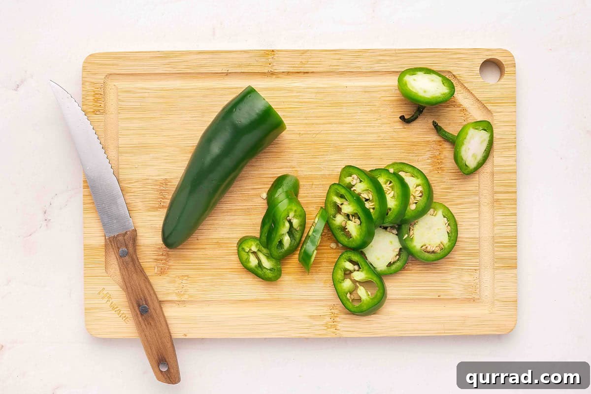 Cowgirl Candy Jalapeno Pepper Jelly Recipe 5 Half a jalapeno on a wooden cutting board with jalapeno slices next to it.