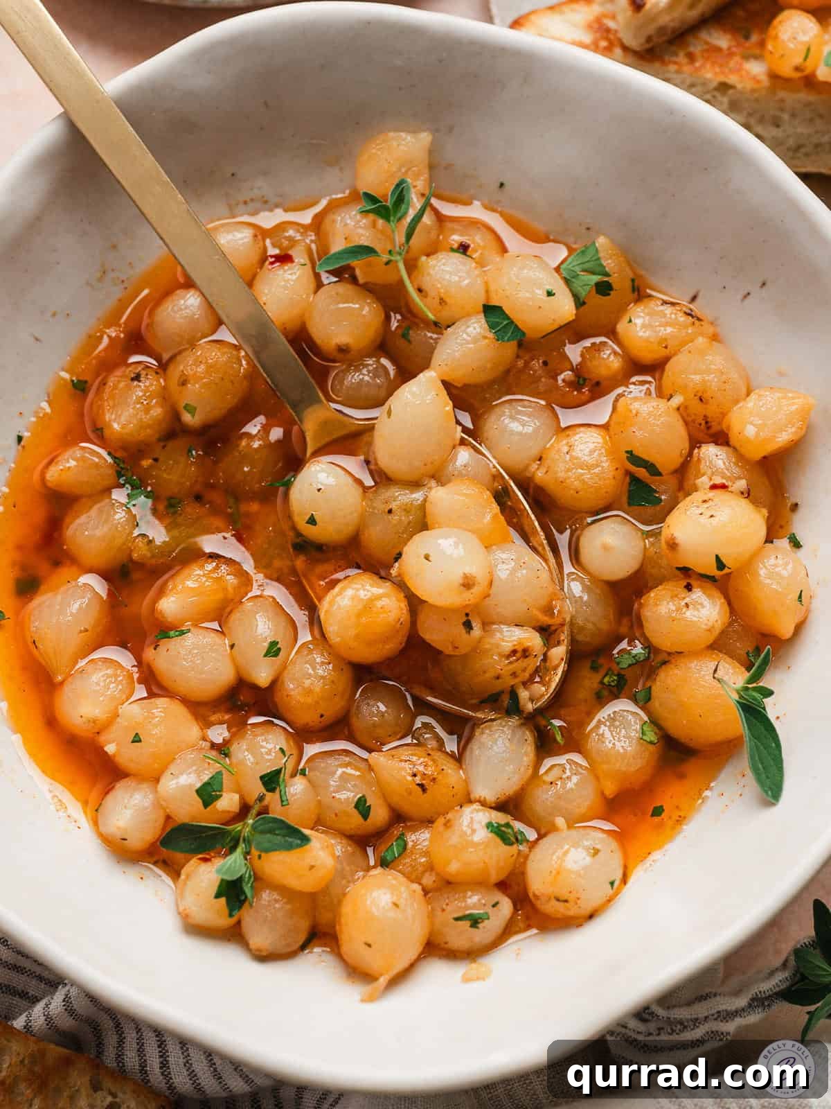 One-Pot Mini Pearl Onion Boil with Garlic and Herbs 2 Overhead view of a mini pearl onion bowl in a bowl with a spoon.
