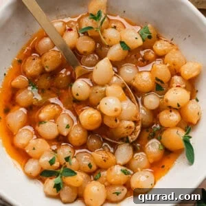 One-Pot Mini Pearl Onion Boil with Garlic and Herbs 3 Overhead view of a mini pearl onion bowl in a bowl with a spoon.