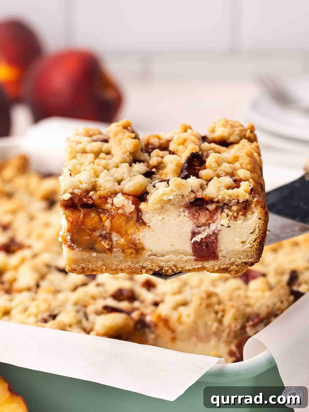 Irresistible Peach Cobbler Cheesecake Bars 2 Side view of a peach cobbler cheesecake bar being lifted out of a baking dish.