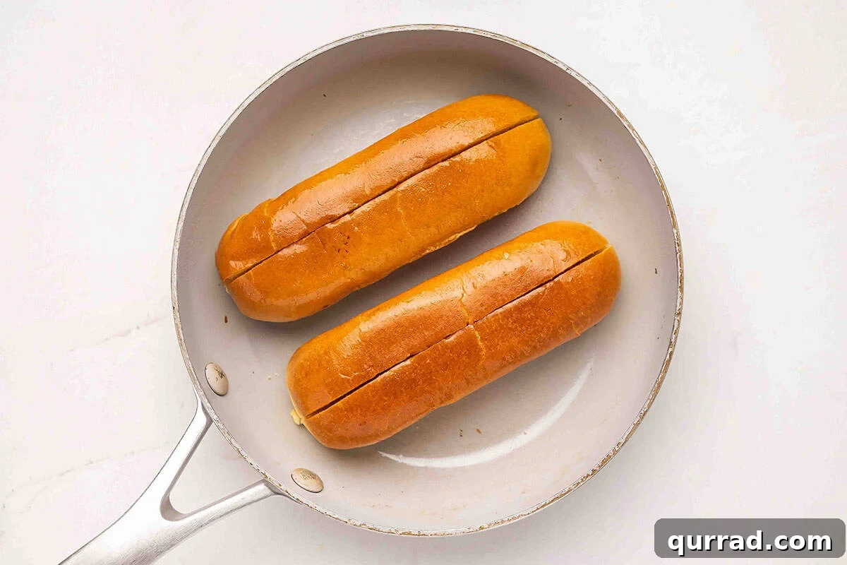 Brioche hot dog rolls toasting in a skillet.