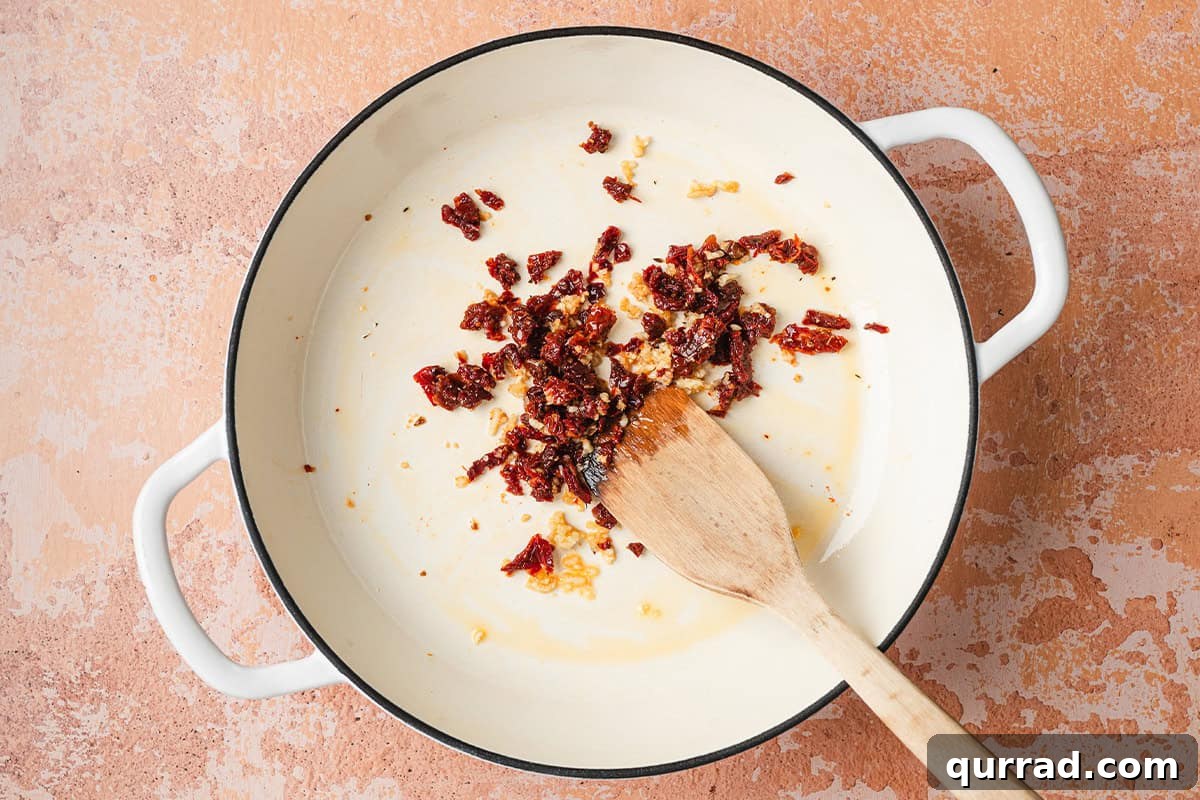Marry Me Beans: Creamy Tomato and Herb Skillet 5 Minced garlic and sun dried tomatoes in a skillet with a wooden spatula.