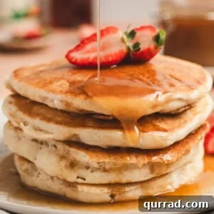 A stack of pancakes topped with maple butter syrup and strawberry halves.