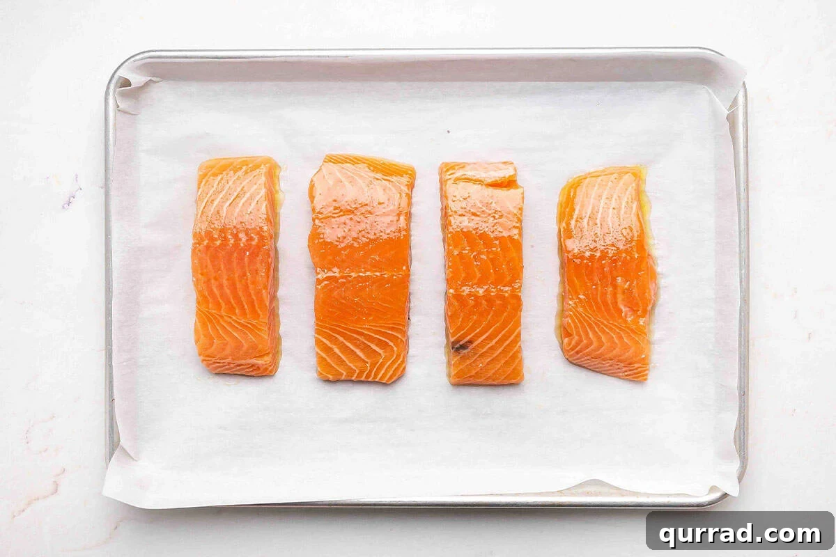 Sticky Brown Sugar-Glazed Salmon Recipe 6 Four salmon filets coated in olive oil on a parchment lined baking sheet.