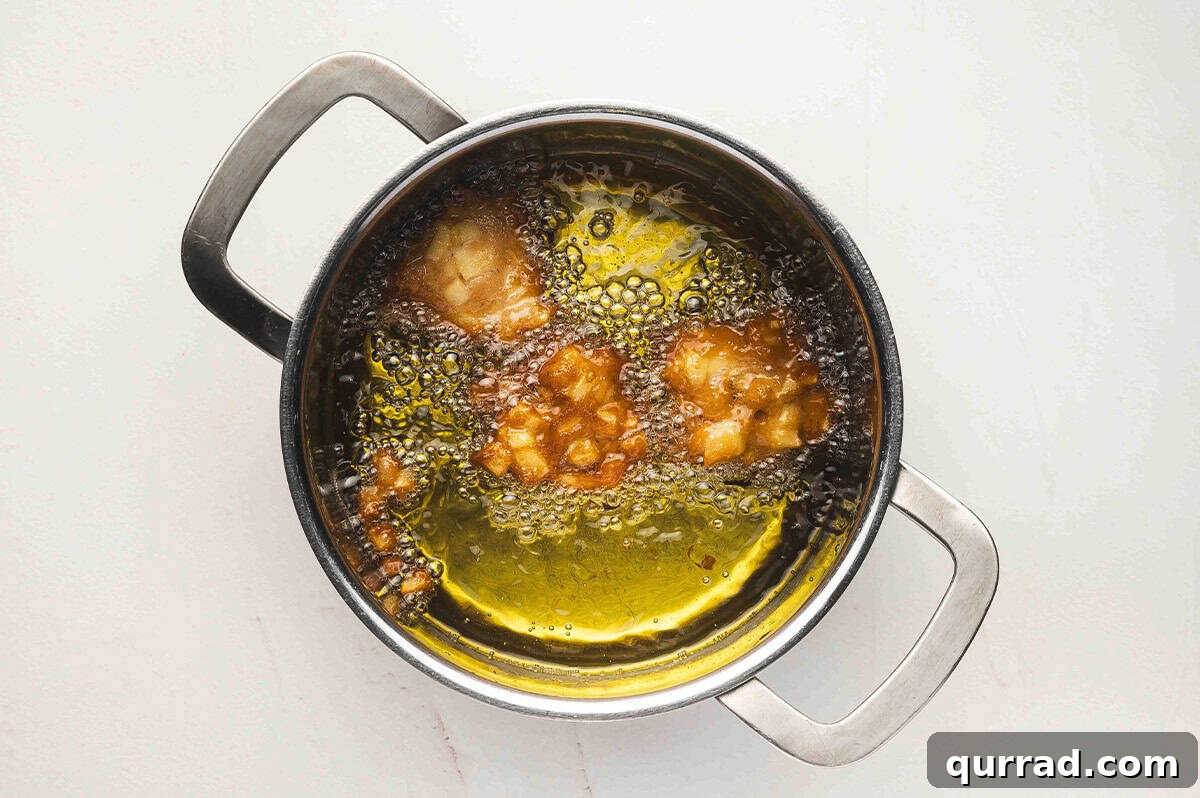 A pot of hot oil with several spoonfuls of apple fritter batter frying and bubbling.