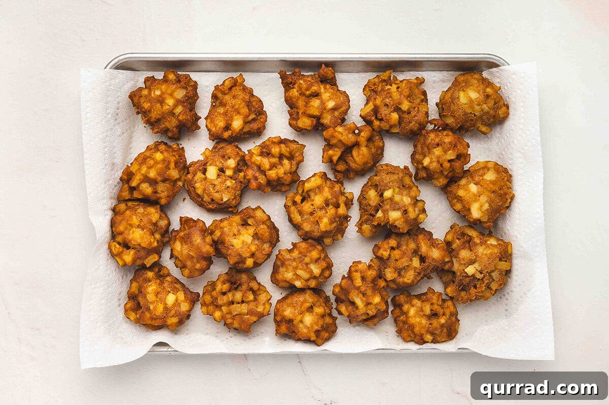 A tray lined with paper towels holding freshly fried apple fritters cooling.