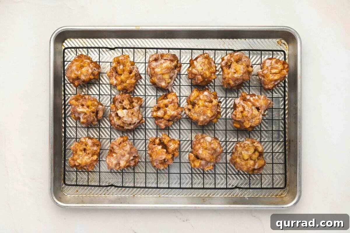 Freshly glazed apple fritters cooling on a wire rack set over a baking sheet.